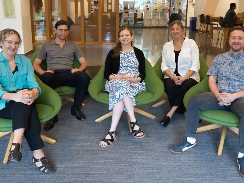 The five full-time ATLIS team members sit in green chairs in the Milstein Lobby, smiling and looking at the camera